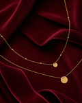 Collier doré à double chaîne et médailles sur fond rouge signature Amani by Layal